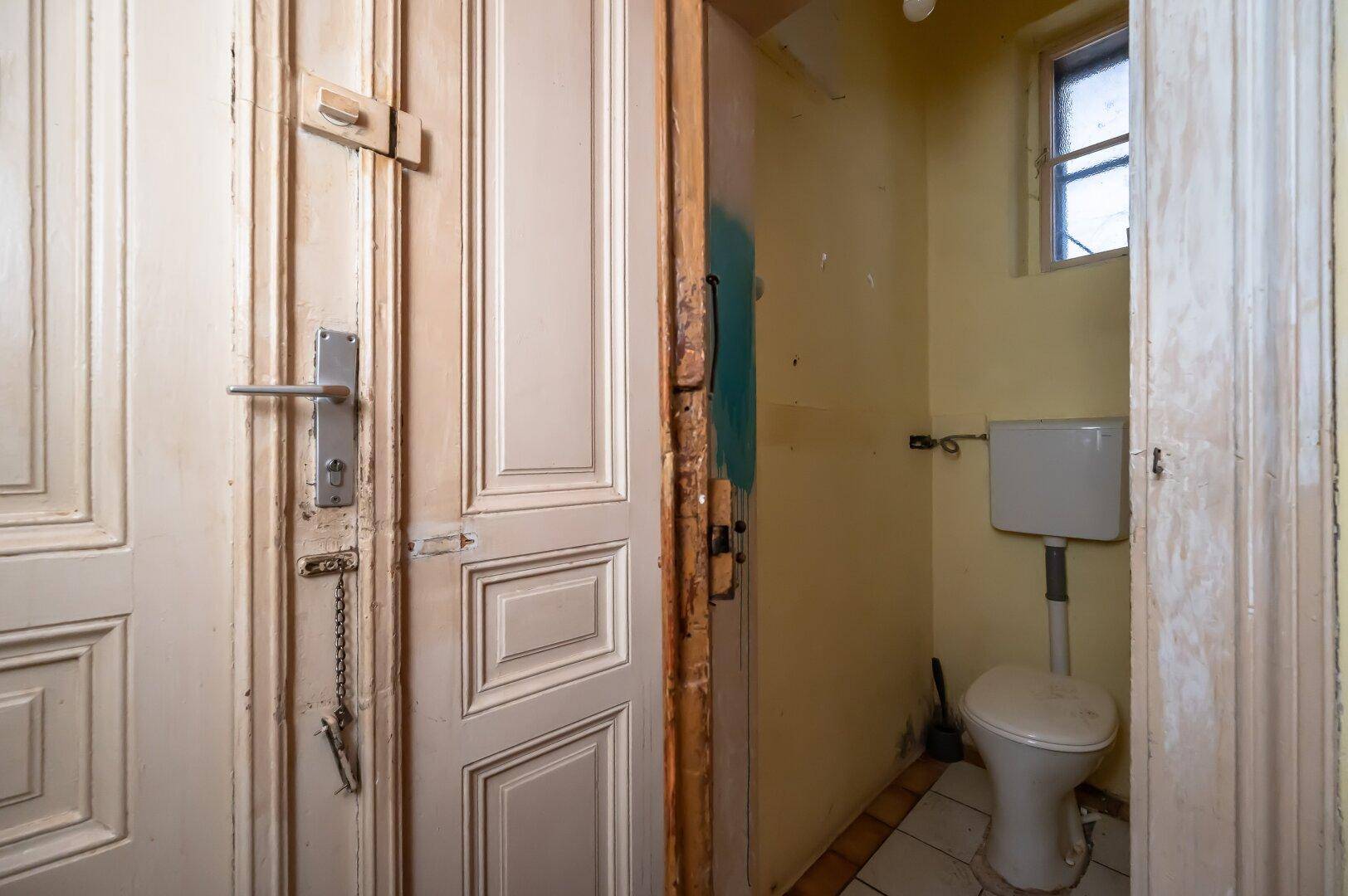 Kleines WC mit Toilette, Fliesenboden und einem kleinen Fenster für Belüftung.