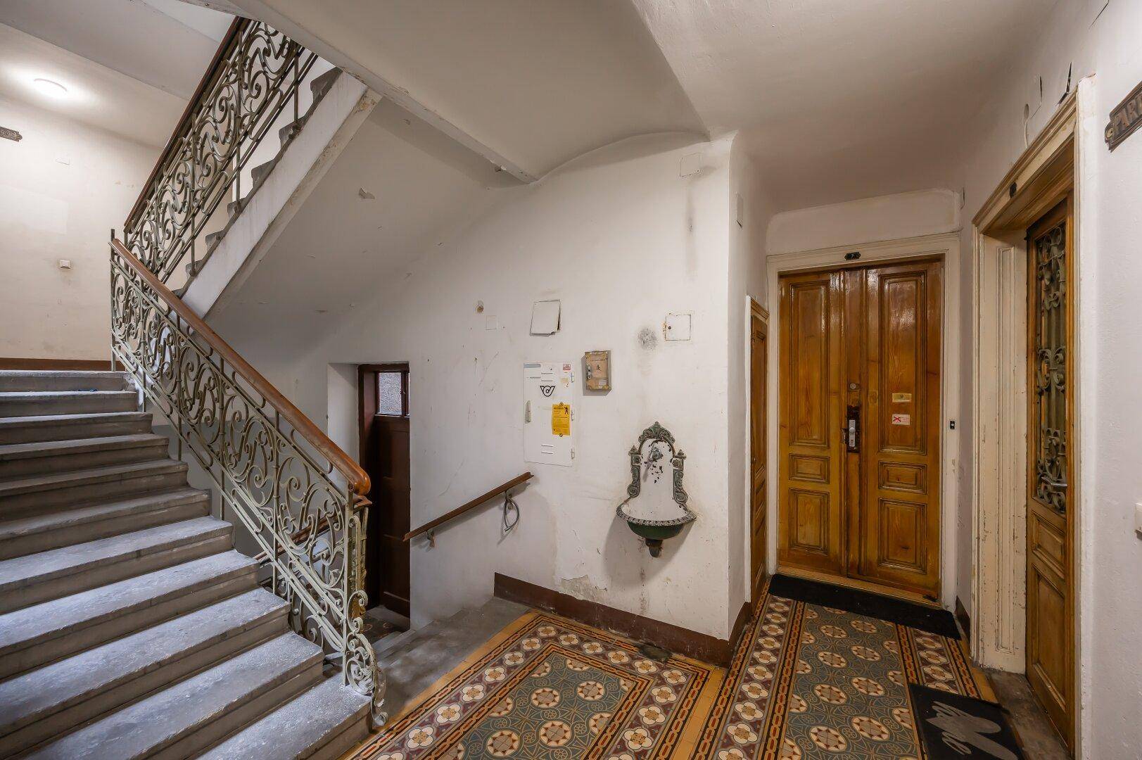 Historisches Treppenhaus mit schmiedeeisernem Geländer, Steinstufen und gemusterten Teppichläufern.