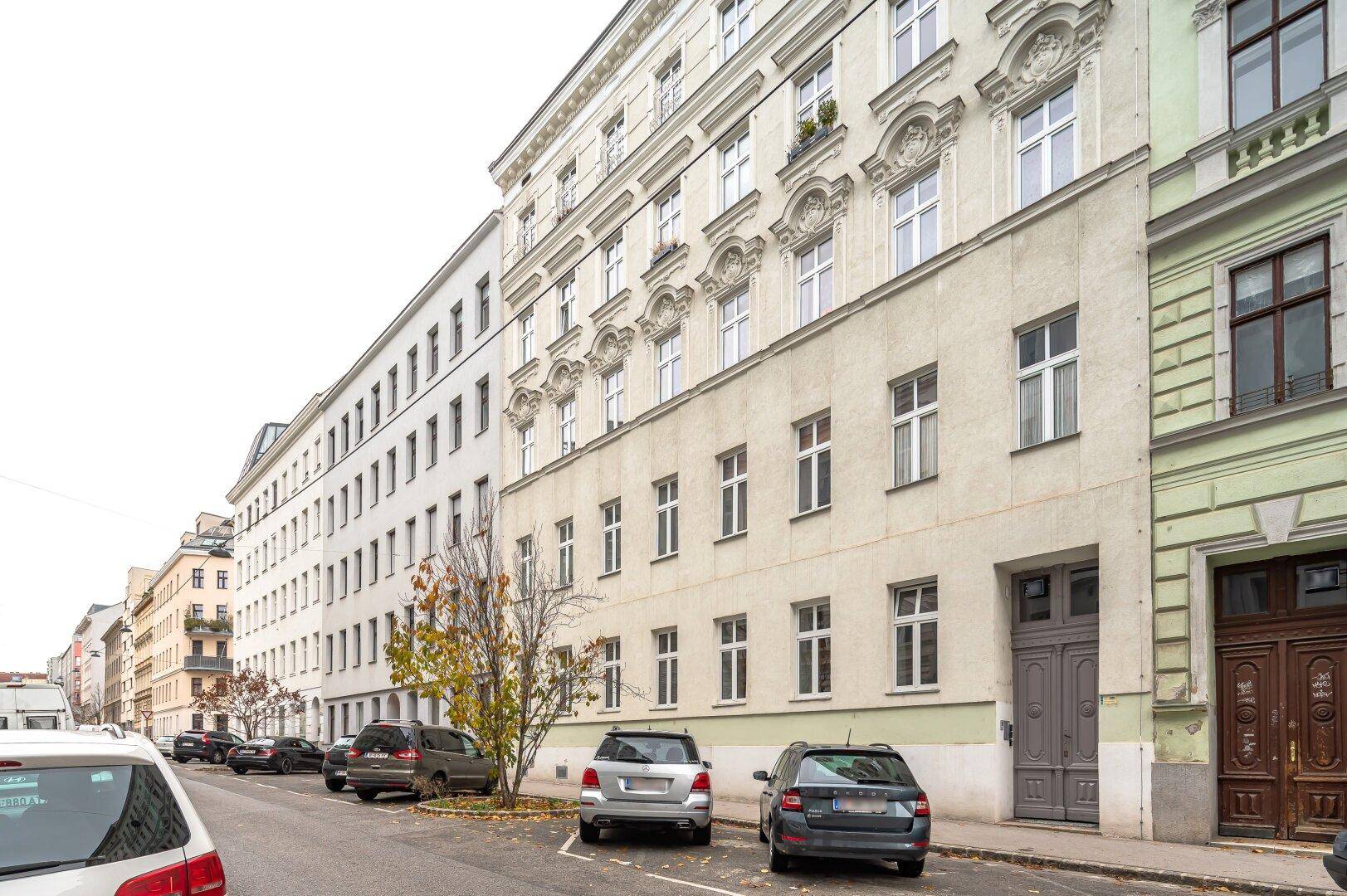 Historisches Gebäude mit klassischer Fassade und parkenden Autos auf der Straße.