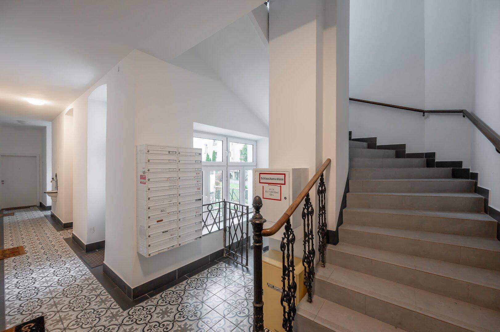 Heller Eingangsbereich mit dekorativen Fliesen, Briefkästen und Zugang zur Treppe.