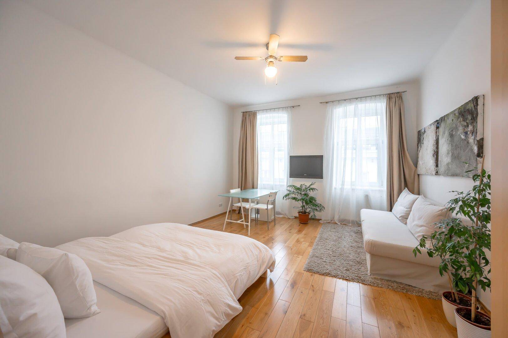 Gemütlicher Wohnbereich mit Holzboden, beigem Sofa und einem kleinen Esstisch, ideal für ein Studio-Apartment.