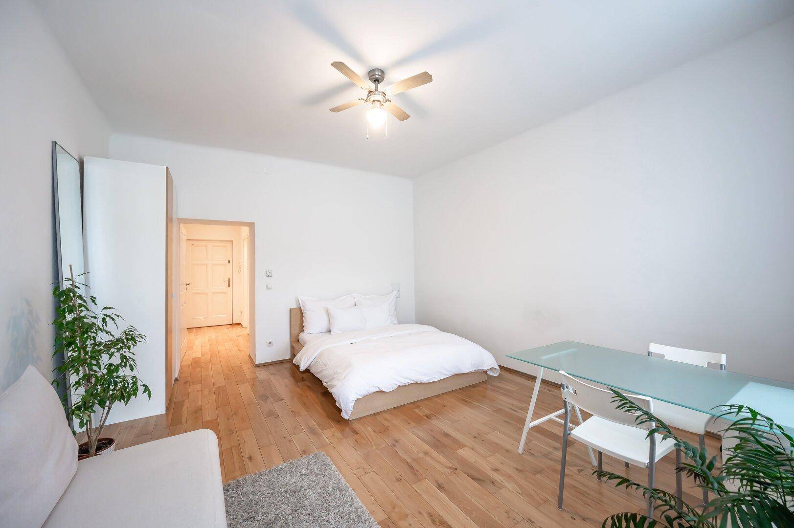 Geräumiges Zimmer mit Holzboden, Bett, Sofa und Esstisch, ideal für ein Studio-Apartment.