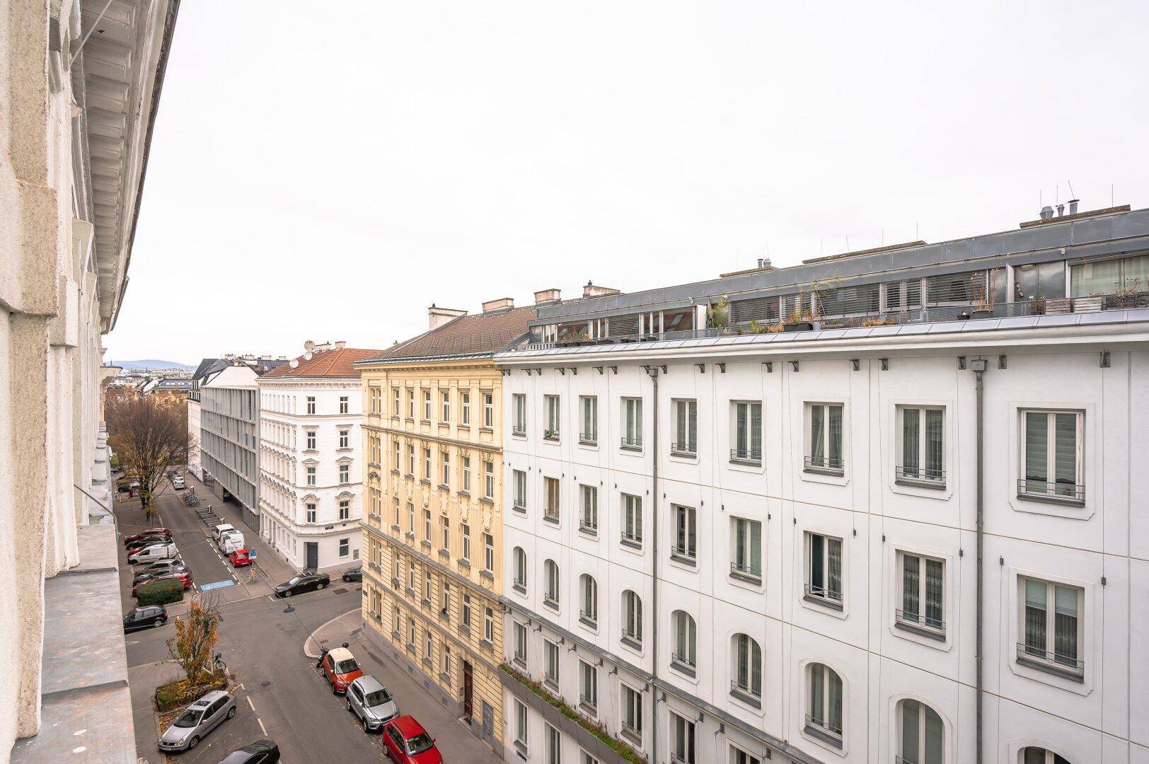 Weitläufiger Blick über eine städtische Straße mit historischen Gebäuden und parkenden Autos.