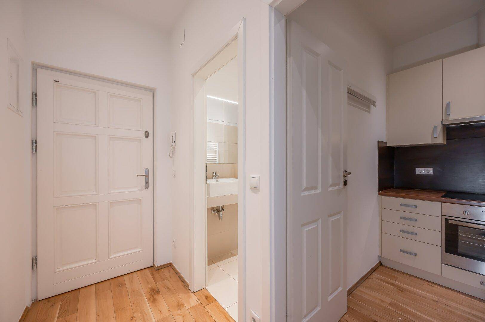Eingangsbereich mit Holzboden, der zur Küche und zum modernen Badezimmer führt.