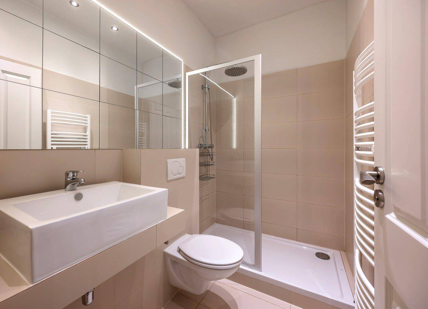 Modernes Badezimmer mit beigen Fliesen, ebenerdiger Dusche, wandhängendem WC und beheiztem Handtuchhalter.