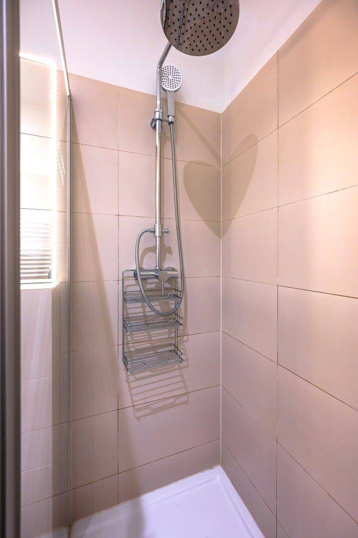 Moderne Dusche mit Regenduschkopf und beigen Fliesen, bietet Komfort und Stil.