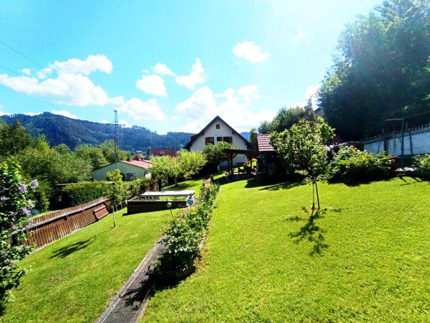 Weitläufiger Garten mit Rasenfläche, Bäumen und Blick auf die umliegende Hügellandschaft.