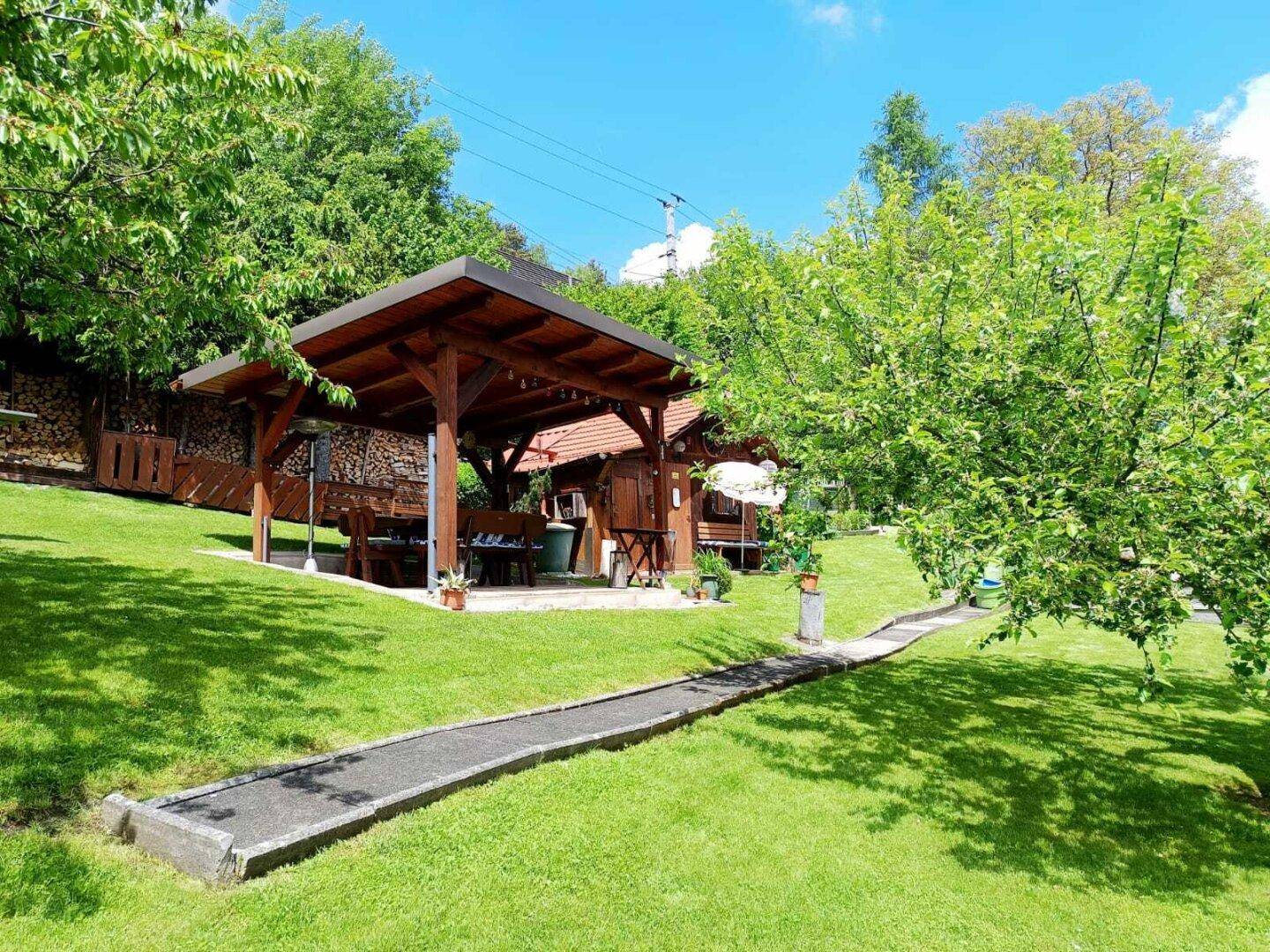 Großer Garten mit Rasenfläche, Bäumen und einem überdachten Sitzbereich.