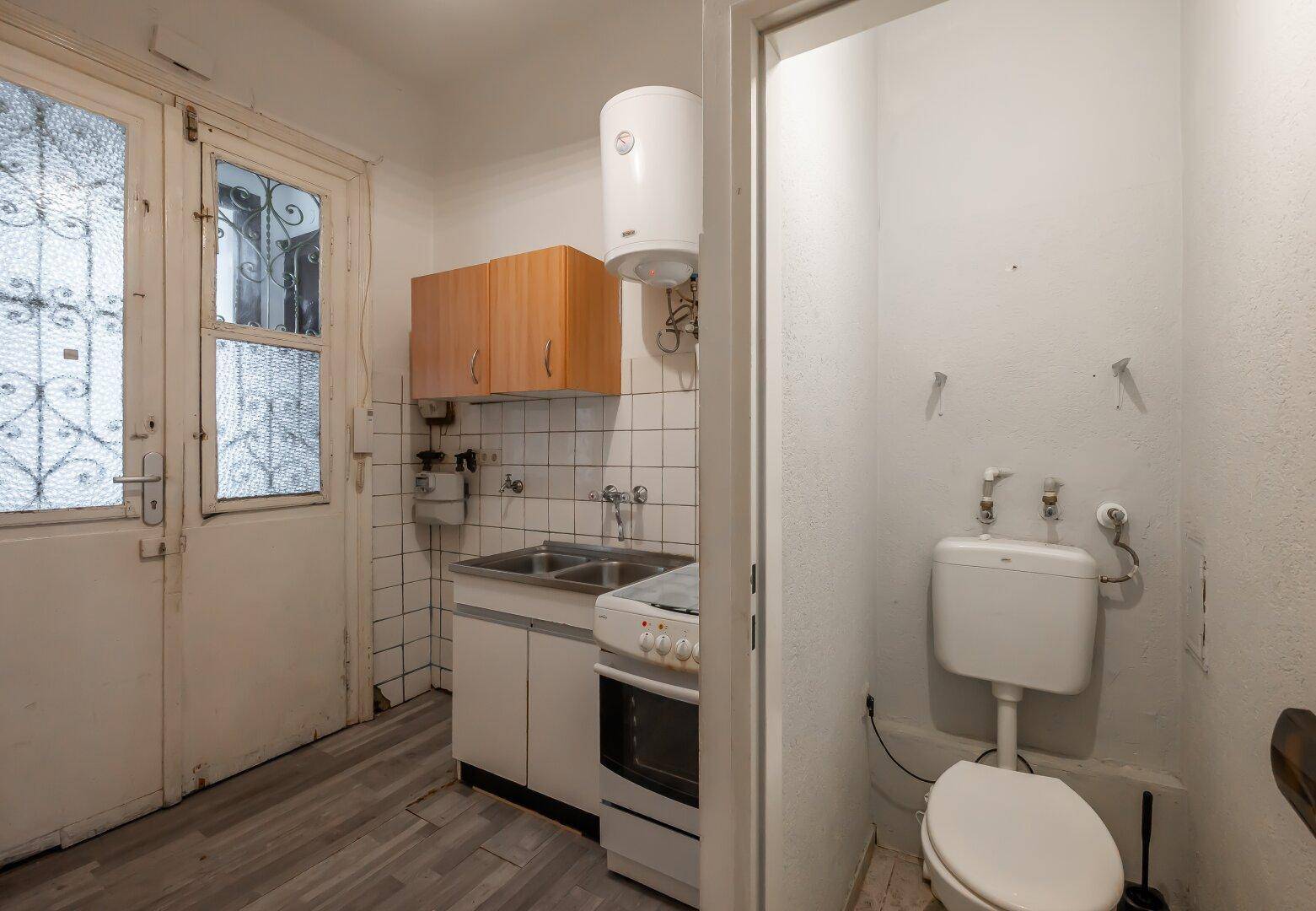Kleine Küche mit Herd und Spüle, angrenzend an eine separate Gästetoilette.
