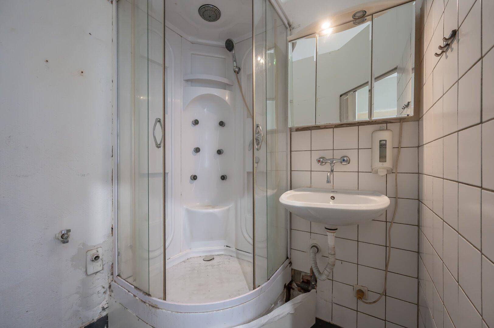 Detaillierte Ansicht der Duschkabine und des Waschbeckens in einem kleinen Badezimmer.