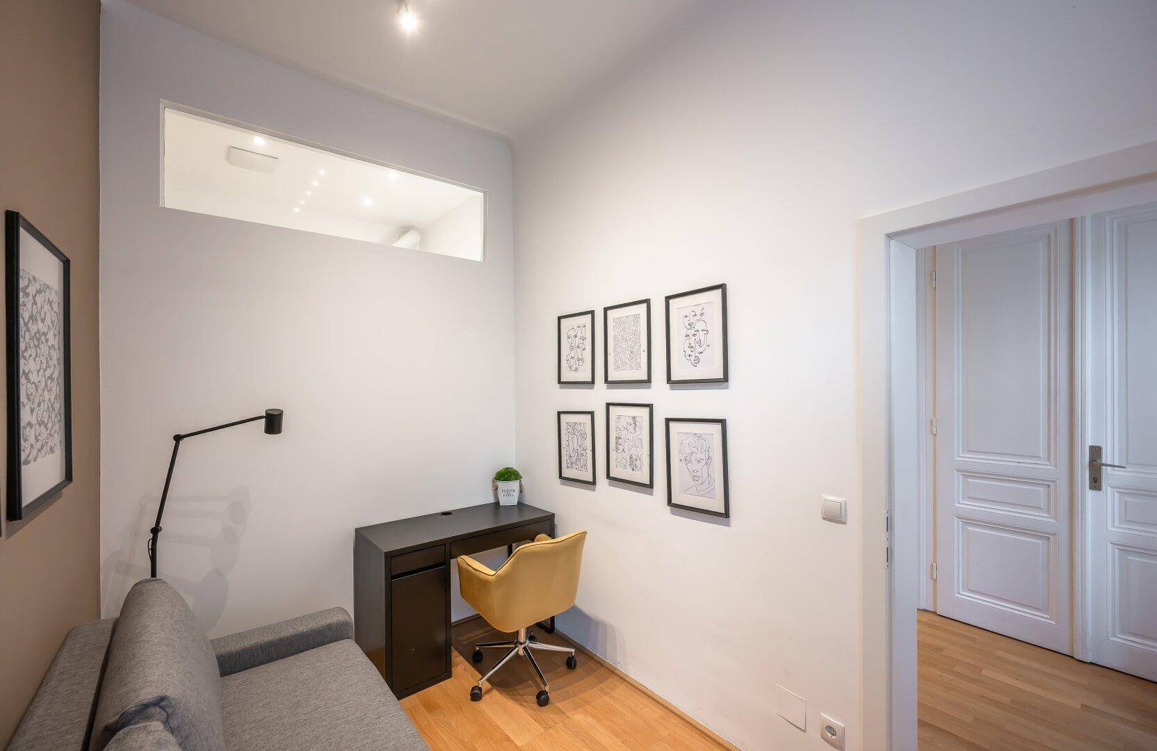 Kleines Arbeitszimmer mit Schreibtisch, Sofa und Holzboden, ideal für Home-Office.