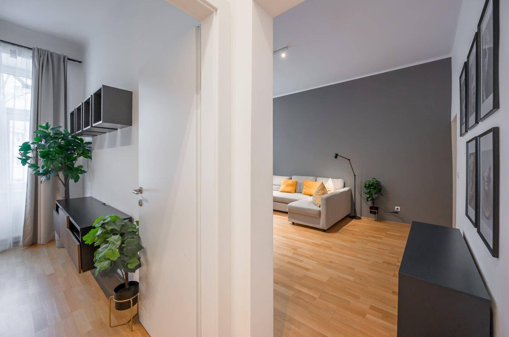 Blick vom Flur in das helle Wohnzimmer mit Holzboden und moderner Einrichtung.
