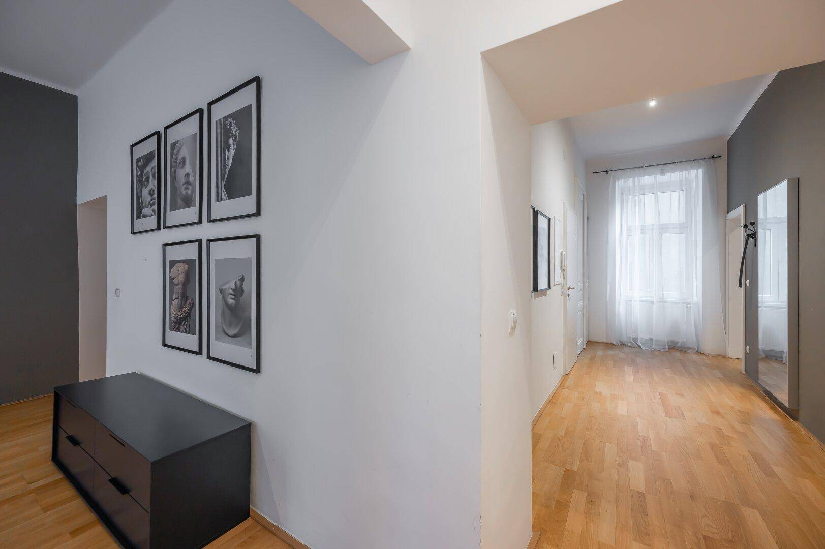 Langer Flur mit Holzboden, Spiegel und Kunstwerken an den Wänden.