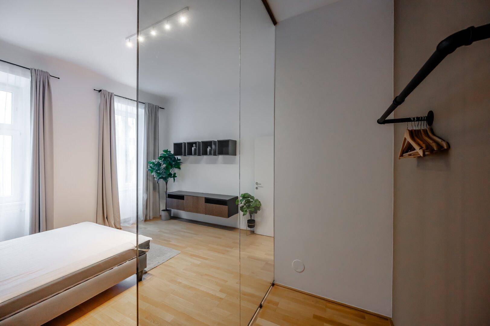 Schlafzimmer mit Holzboden, Spiegelfront und offenem Kleiderständer.