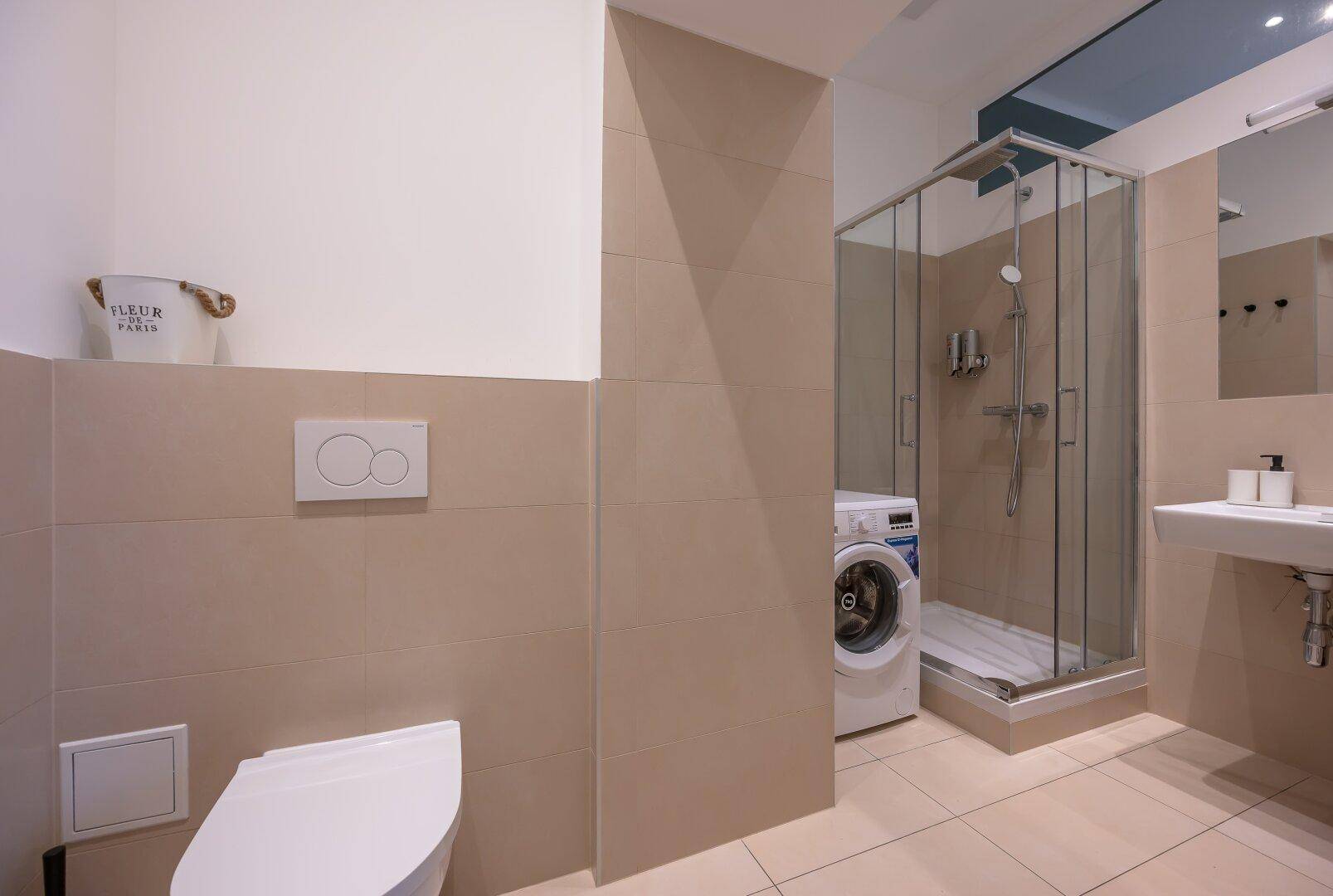 Modernes Badezimmer mit Duschkabine, WC, Waschbecken und integrierter Waschmaschine.