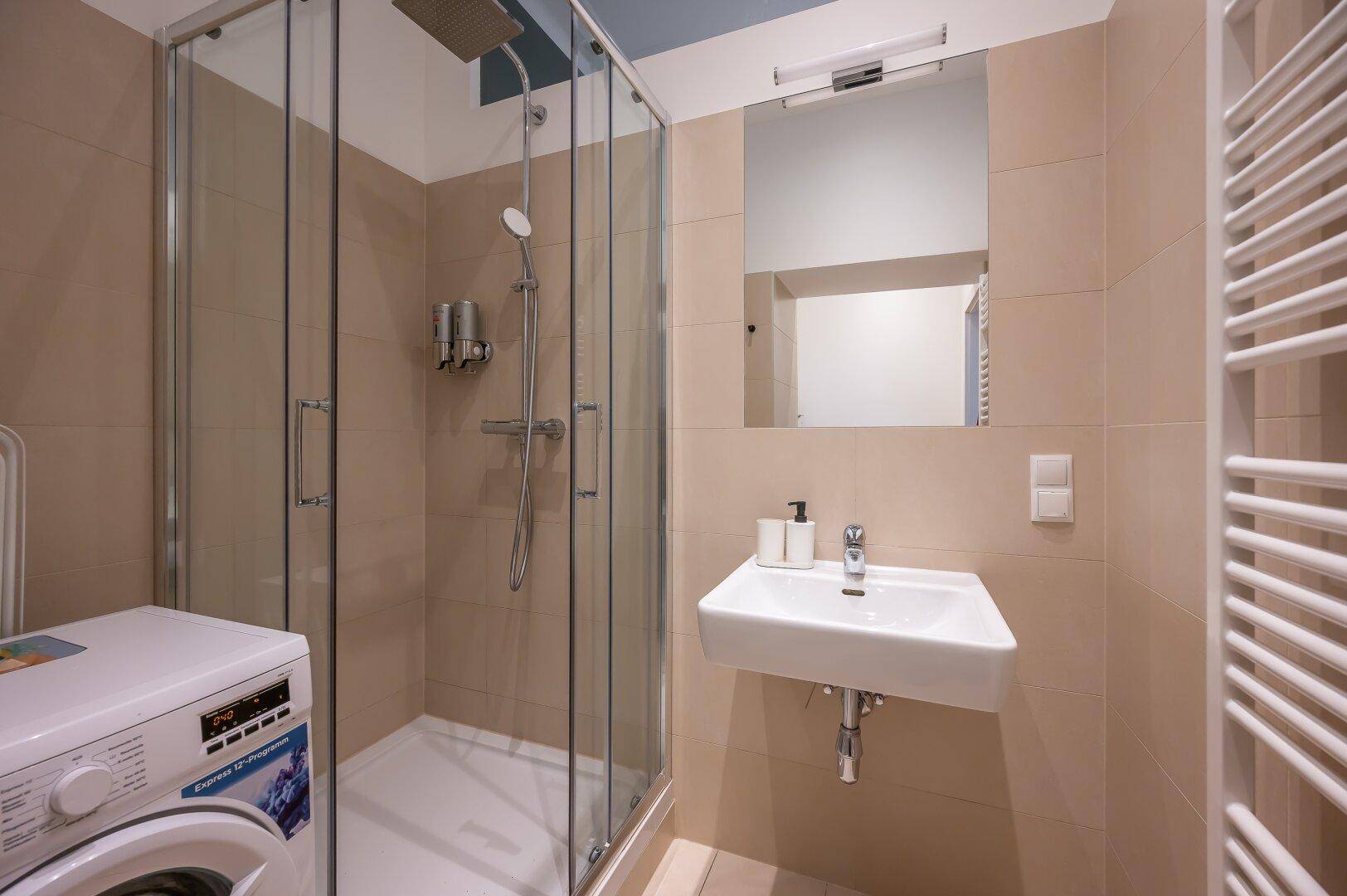 Helles Badezimmer mit Duschkabine, Waschbecken, Spiegel und beheiztem Handtuchhalter.