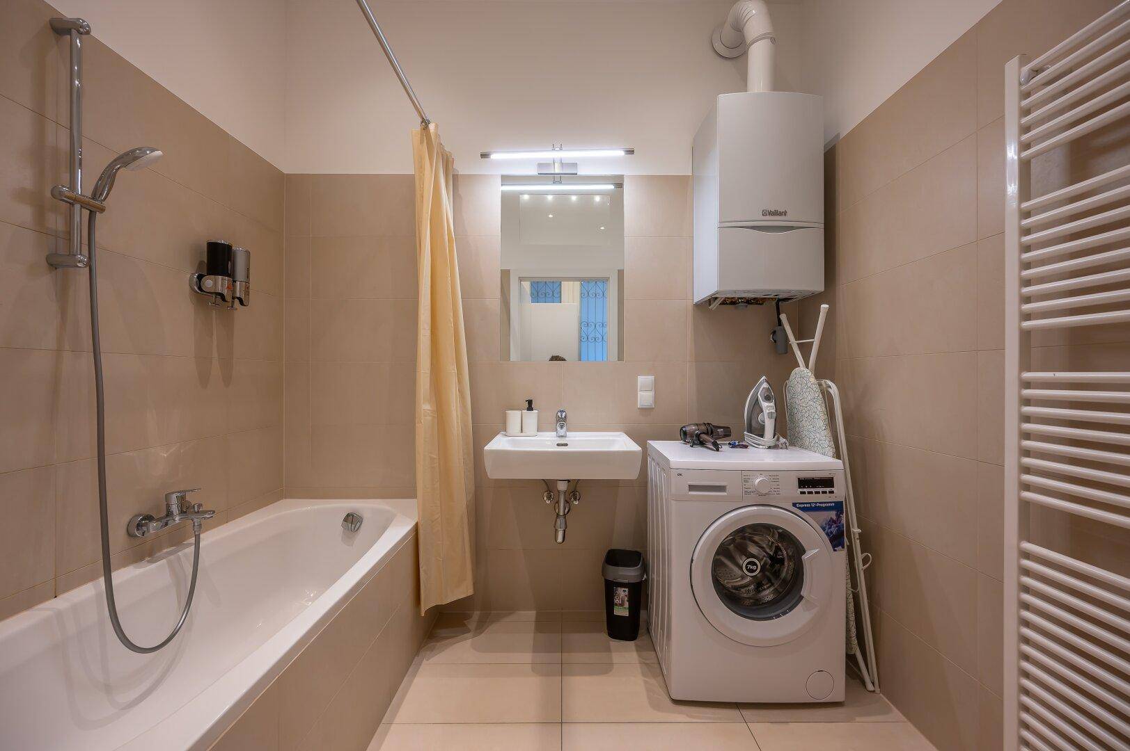 Badezimmer mit Badewanne, Duschvorrichtung, Waschmaschine und beheiztem Handtuchhalter.
