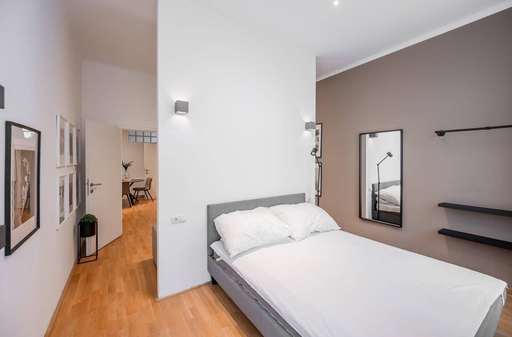 Schlafzimmer mit Doppelbett, Holzboden und indirekter Wandbeleuchtung.