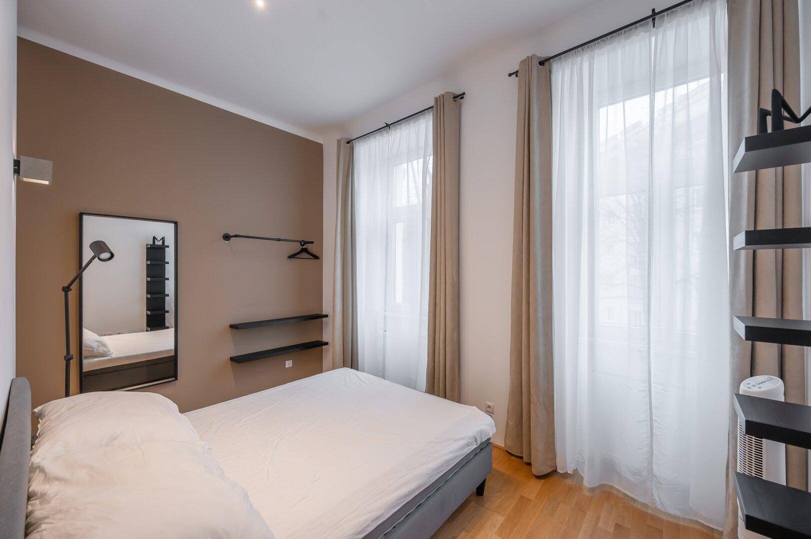 Helles Schlafzimmer mit großen Fenstern, Doppelbett und Holzboden.