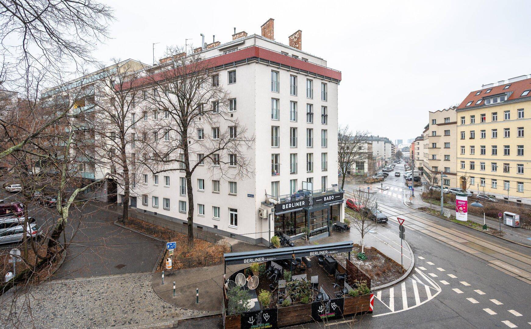 Mehrfamilienhaus in urbaner Umgebung mit Geschäften im Erdgeschoss und Blick auf die Straße.