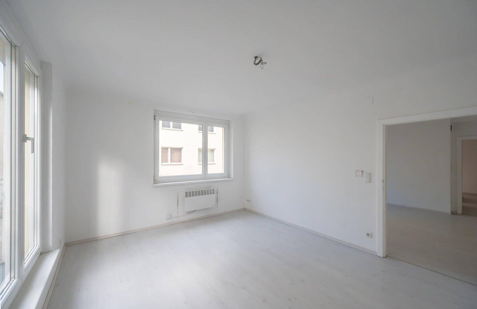 Helles, leeres Zimmer mit weiß gestrichenen Wänden und großen Fenstern, bereit zur individuellen Gestaltung.