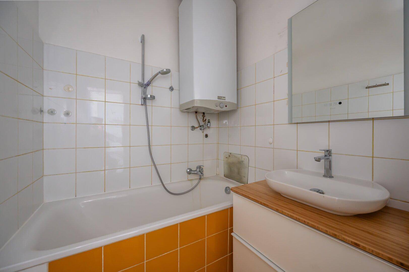 Badezimmer mit Badewanne, gelben Fliesen und einem modernen Aufsatzwaschbecken auf Holzunterschrank.
