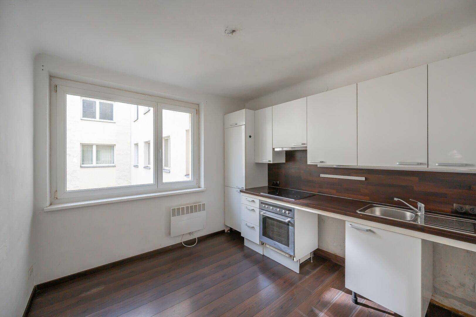Helle Küche mit weißen Oberschränken, dunkler Arbeitsplatte und Fensterblick auf den Innenhof.