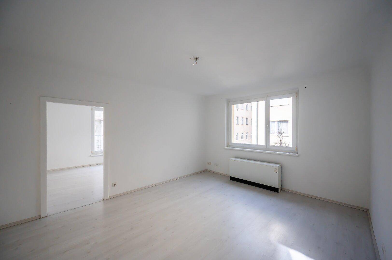 Heller, leerer Raum mit Laminatboden und Blick in ein weiteres Zimmer, ideal für offenes Wohnen.