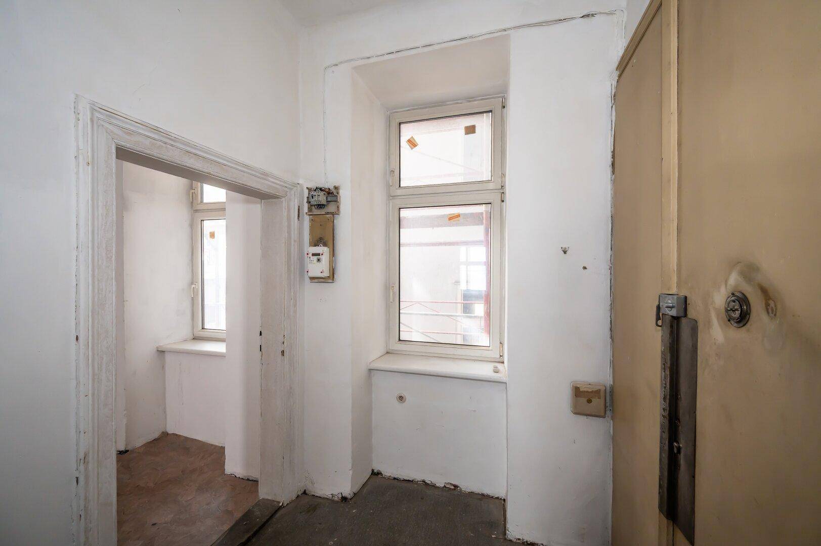 Eingangsbereich mit alter Tür, Fenster und Zählerkasten, zeigt den Renovierungsbedarf.