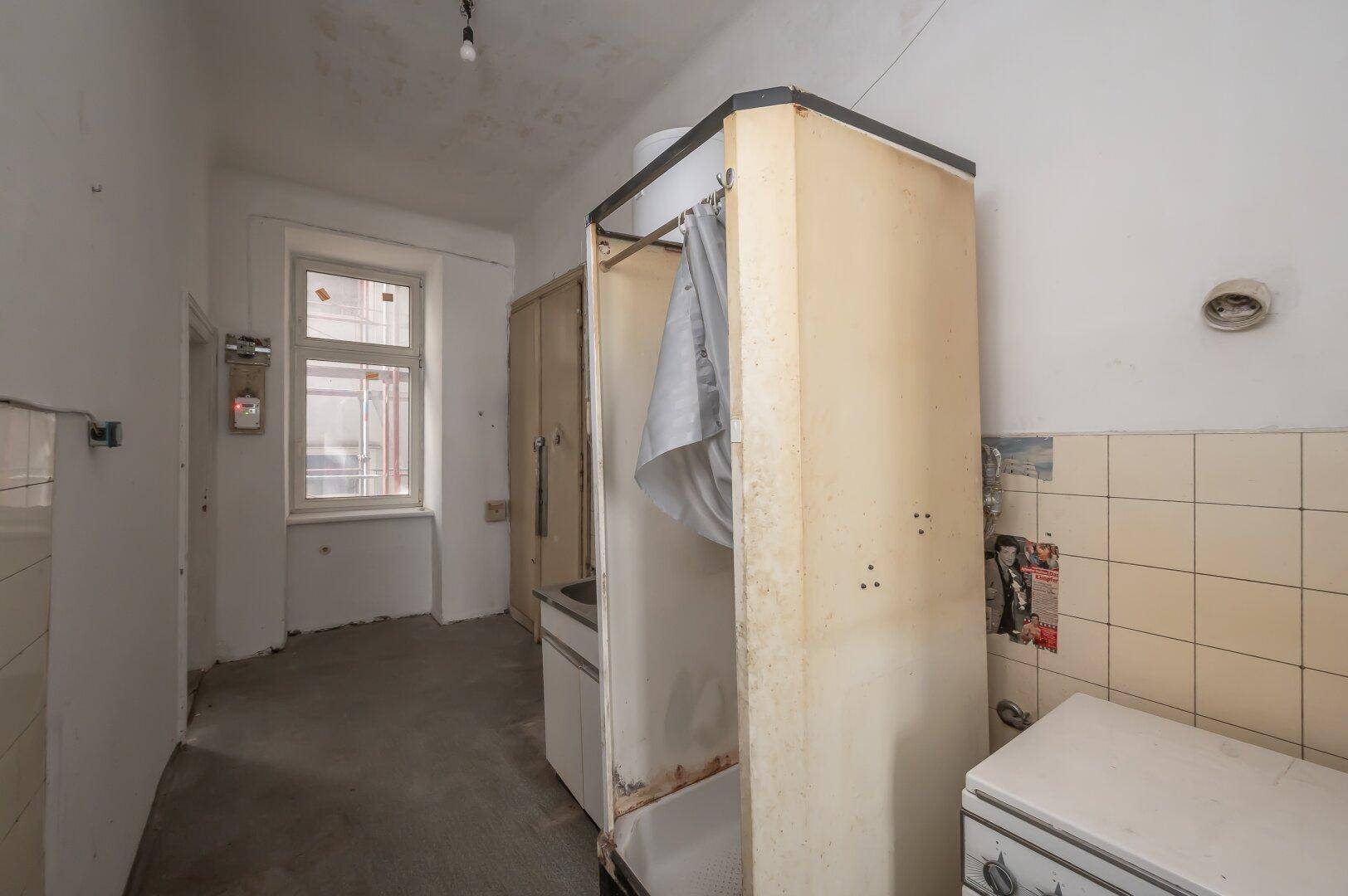 Küche mit alten Geräten, gefliesten Wänden und Fenster, benötigt eine umfassende Renovierung.