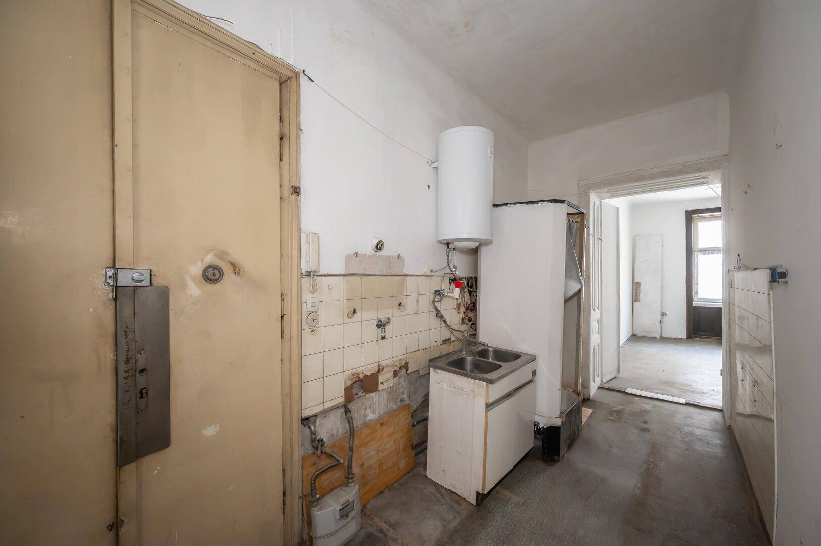 Kleine Küchenzeile mit Spülbecken und Boiler, angrenzend an einen weiteren Raum.