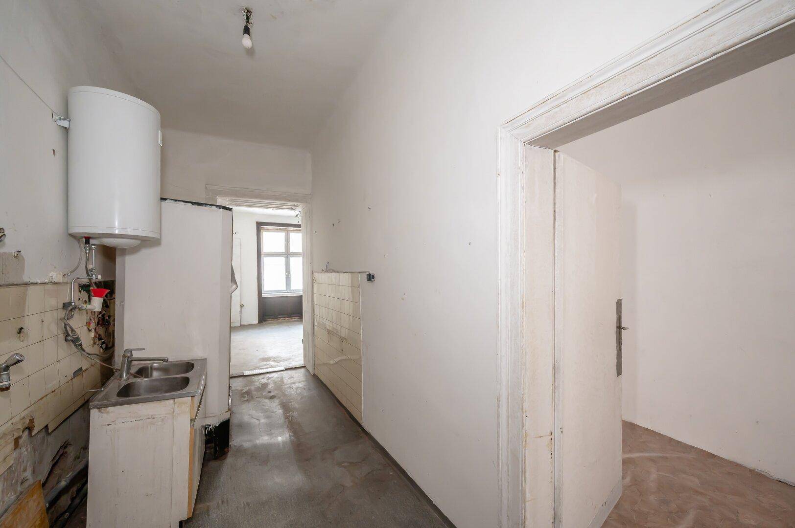Einfache Küchenzeile mit Spüle, Warmwasserboiler und Fliesen, bereit zur Modernisierung.
