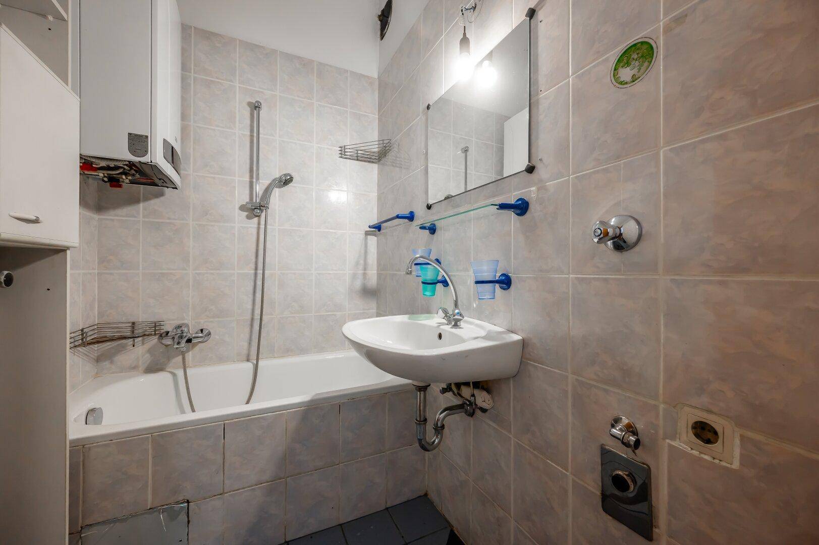 Gefliestes Badezimmer mit Badewanne, Waschbecken und Boiler, in gutem Zustand.