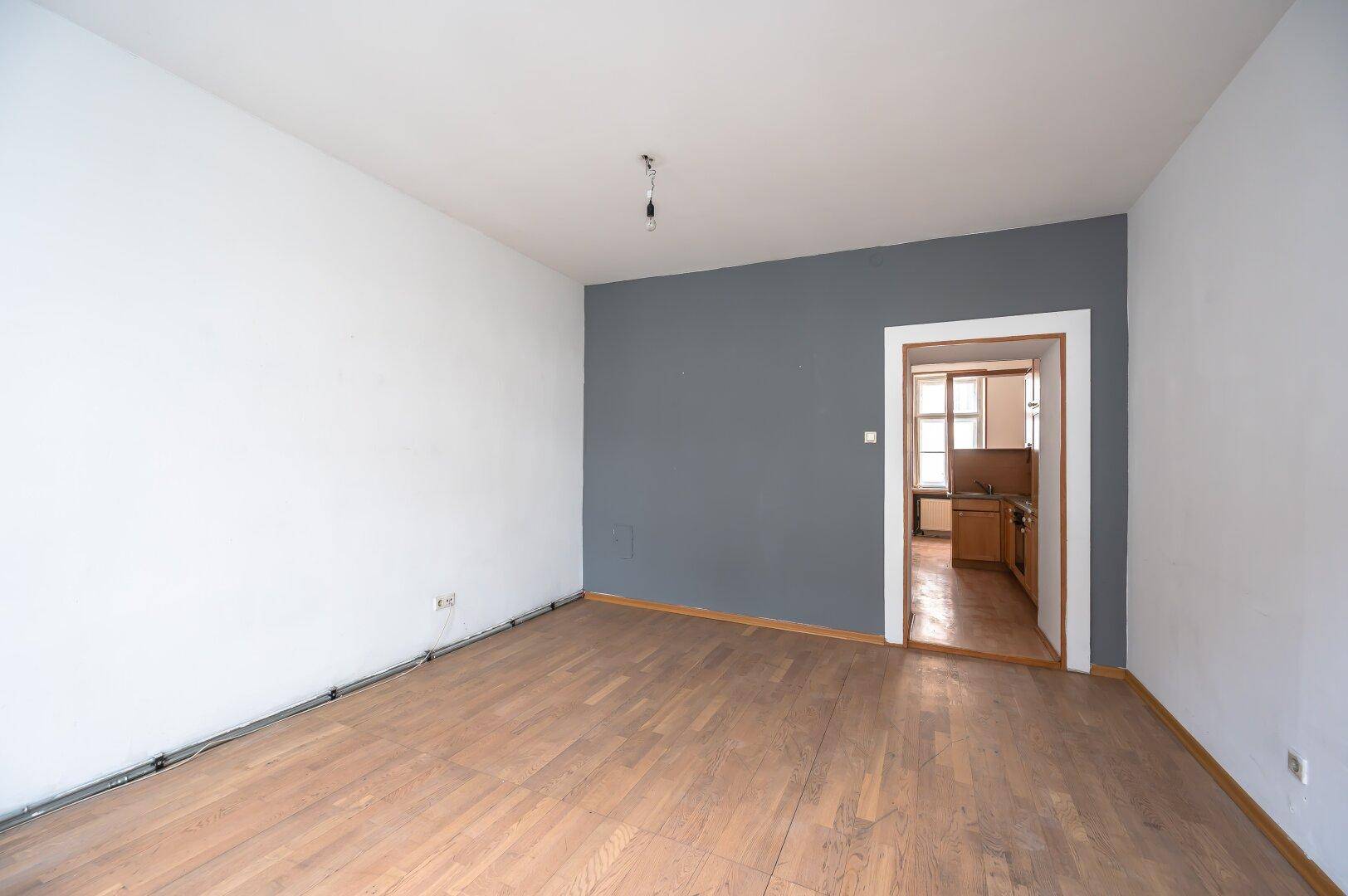Geräumiges Zimmer mit Parkettboden, einer grauen Akzentwand und Zugang zu einem weiteren Raum.