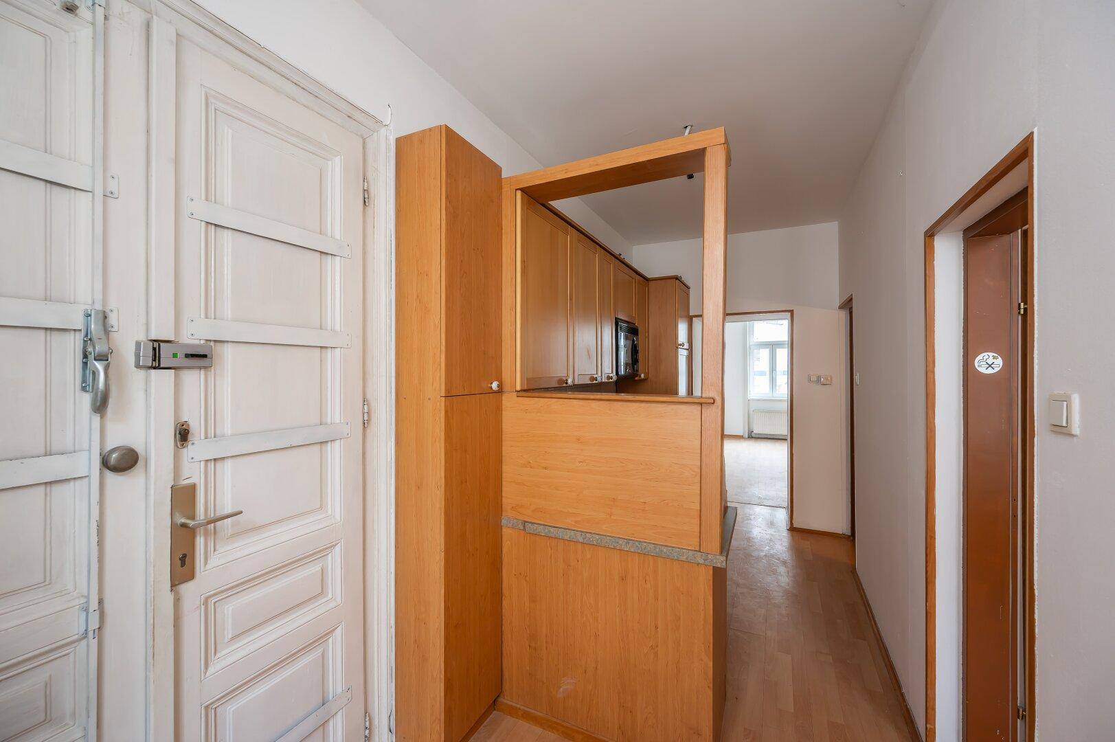 Eingangsbereich mit alter Holztür und Durchgang zur Küche, mit praktischem Holzregal.