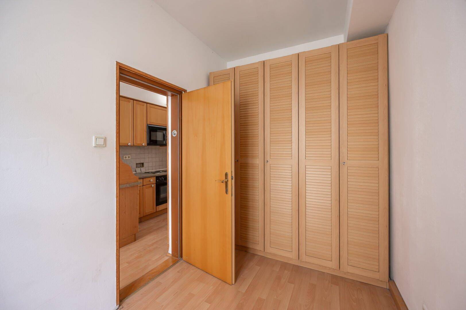 Flur mit eingebautem Holzschrank und Zugang zu einer Küche, mit hellem Holzboden.