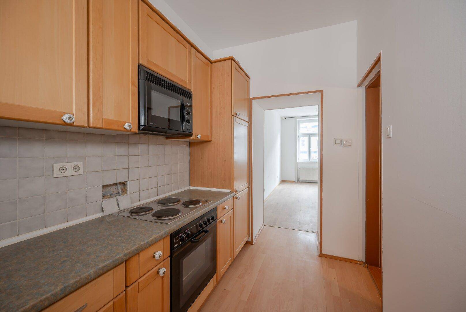 Funktionale Küche mit Holzschränken, Herd und Mikrowelle, mit Blick in ein angrenzendes Zimmer.