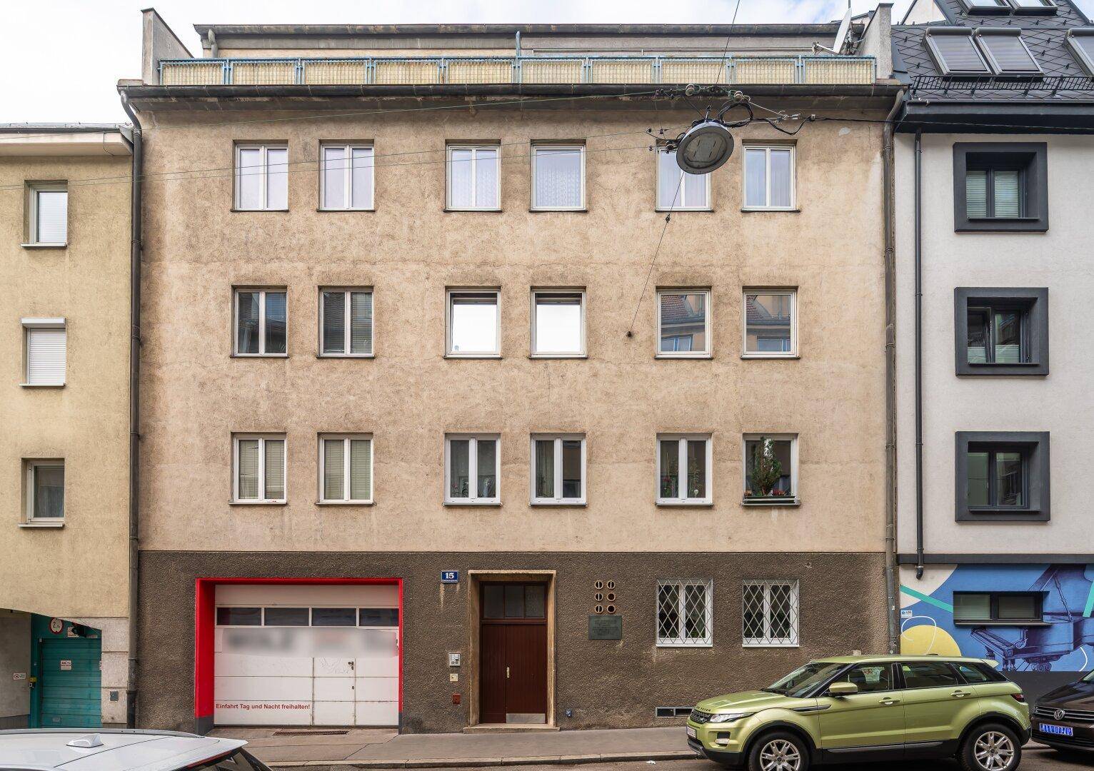 Fassade eines Mehrfamilienhauses mit mehreren Fenstern und einer Garage im Erdgeschoss.