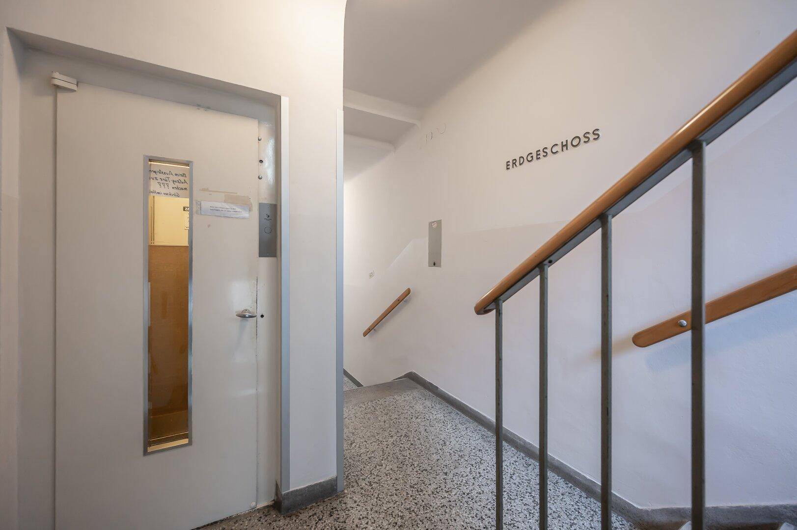 Heller Treppenaufgang mit Terrazzoboden und einem Aufzug für bequemen Zugang zu den Etagen.