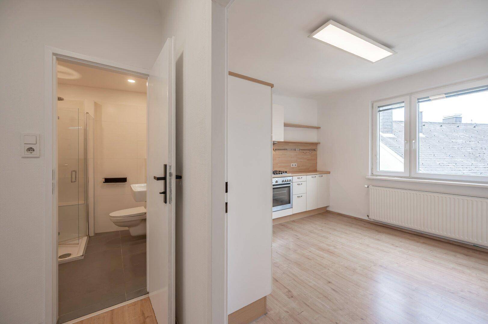 Offener Küchenbereich mit Laminatboden und angrenzendem modernen Badezimmer mit Dusche.