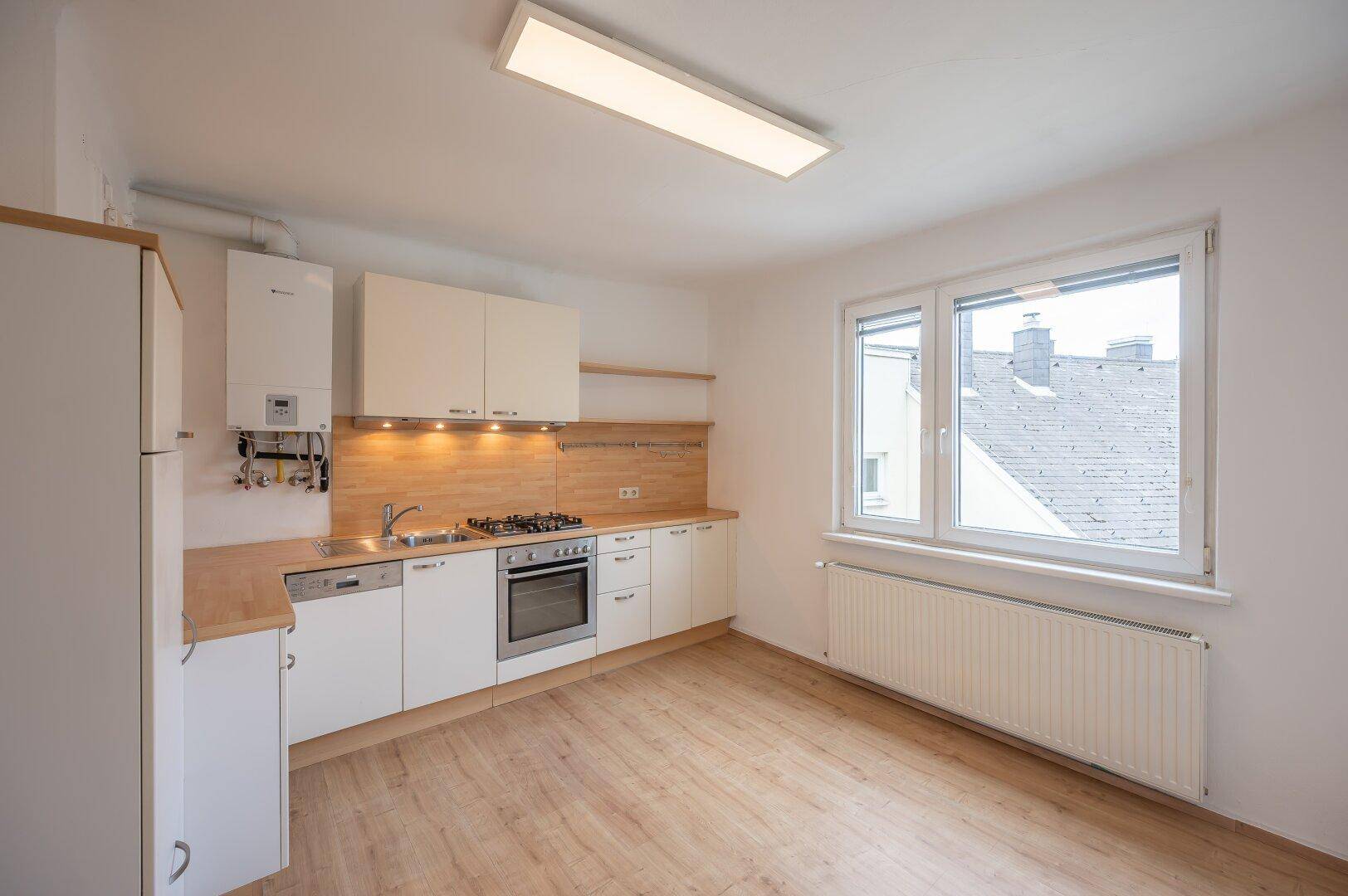 Helle Küche mit weißen Schränken, Holz-Arbeitsplatten und Blick auf die Dächer der Stadt.