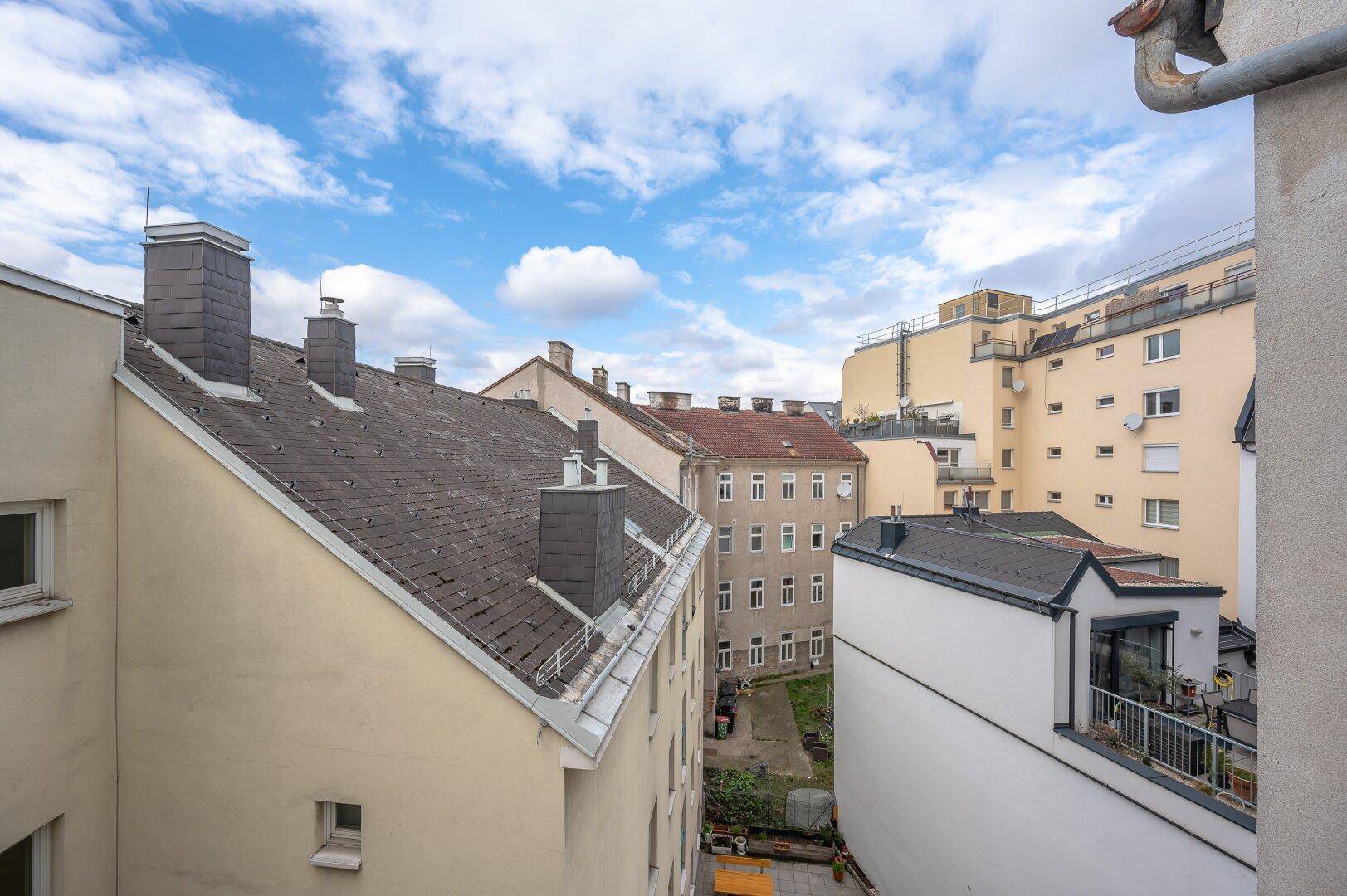 Blick über die Dächer der Stadt mit einem grünen Innenhof und umliegenden Gebäuden.