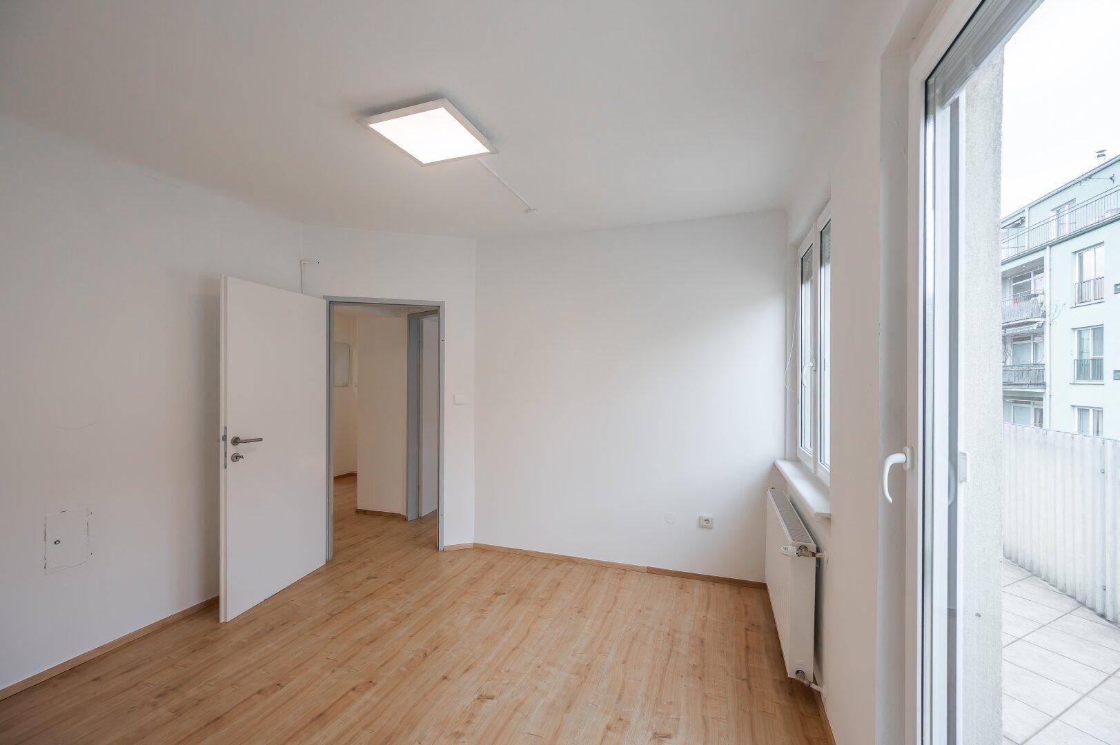 Helles Zimmer mit Laminatboden und direktem Zugang zu einem privaten Balkon.