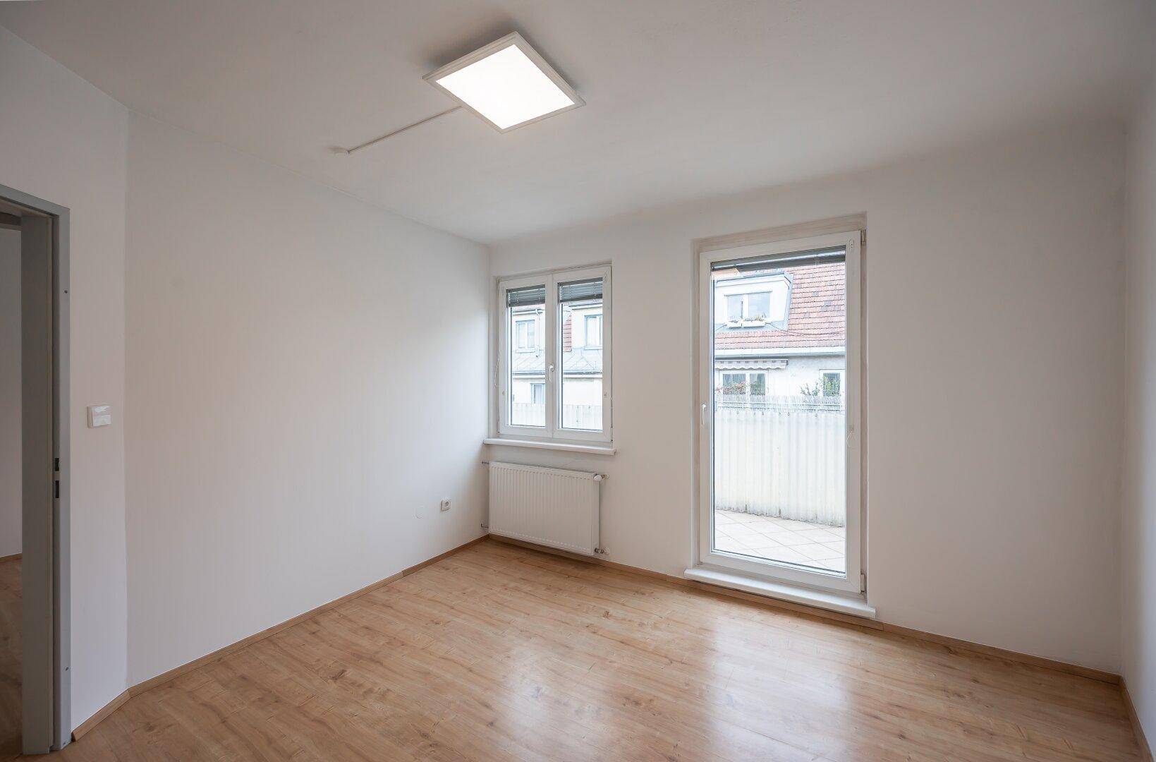 Geräumiges Zimmer mit Laminatboden, zwei Fenstern und Zugang zum Außenbereich.