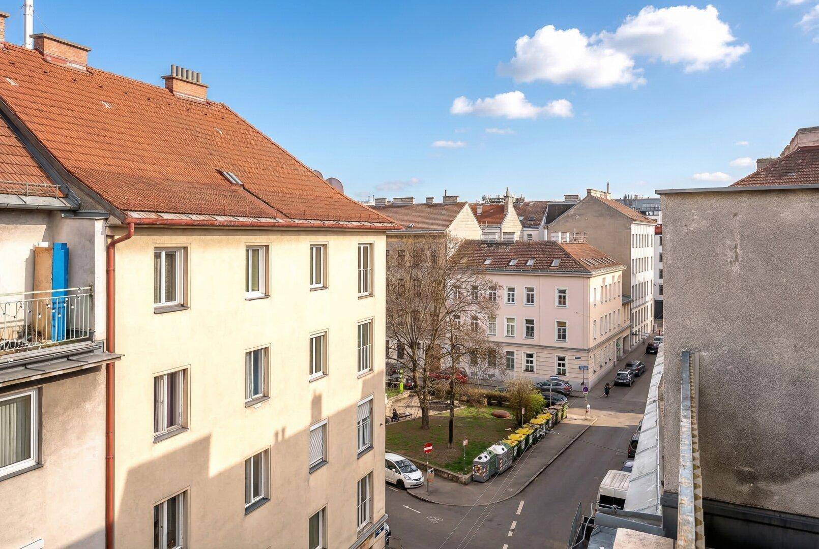 Weitläufiger Blick auf eine ruhige Stadtstraße mit historischen Gebäuden und einem kleinen Park.