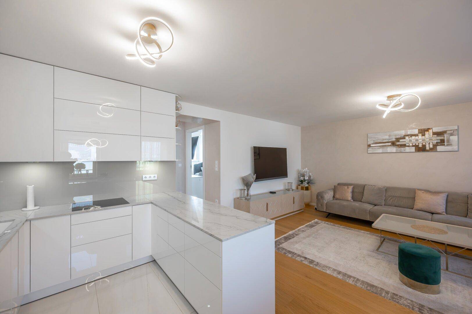 Offener Wohnbereich mit moderner Küche, beigem Sofa und Holzboden.