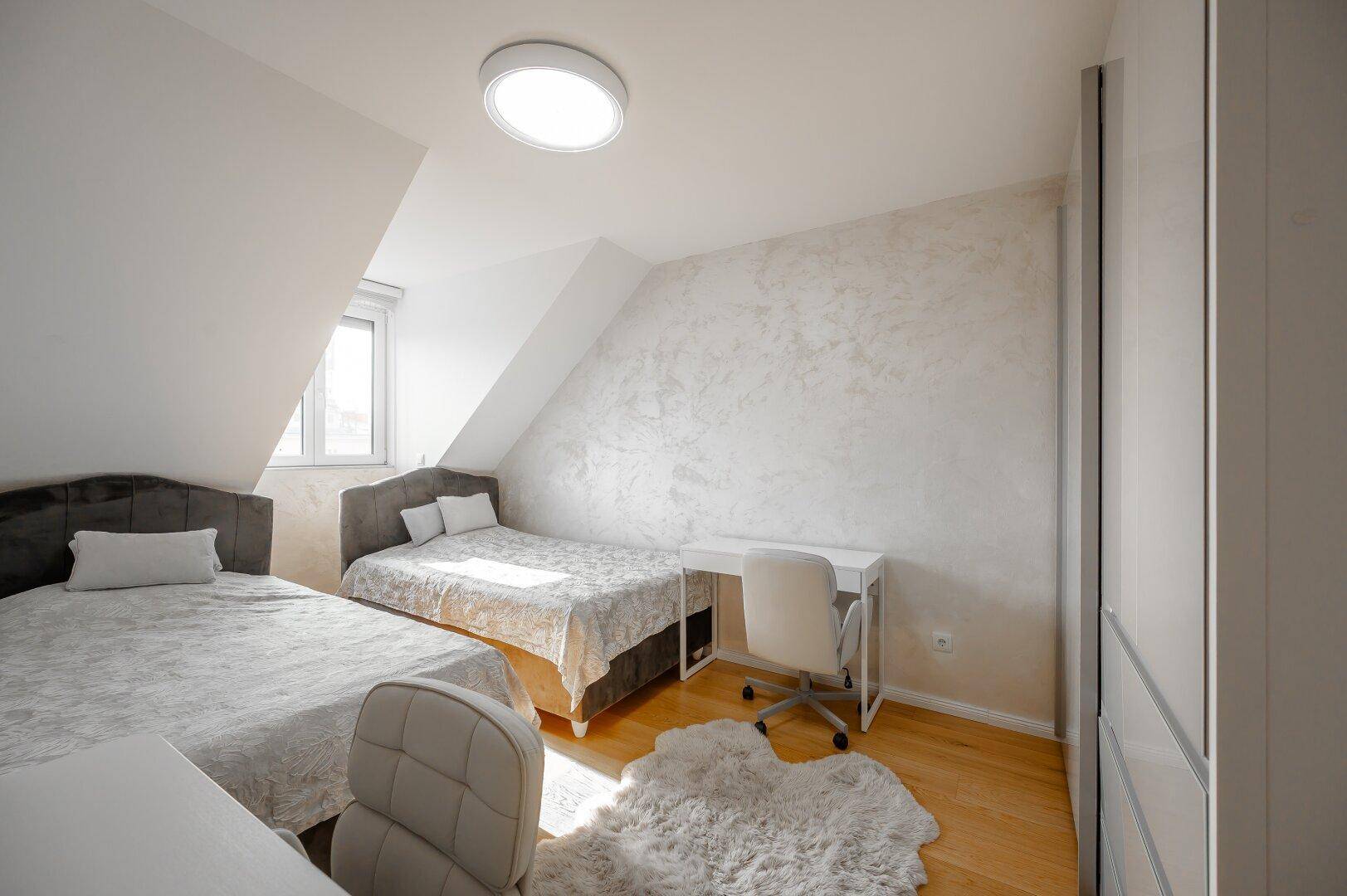 Helles Schlafzimmer mit zwei Betten, Schreibtisch und Dachschräge.