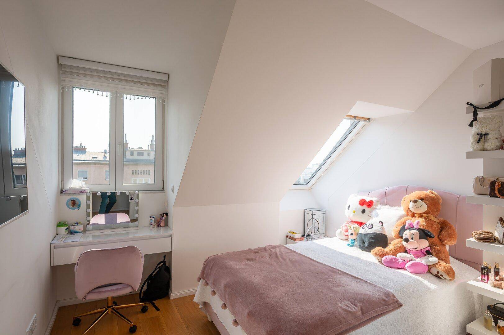 Kinderzimmer mit Einzelbett, Schminktisch und Dachfenster für natürliches Licht.