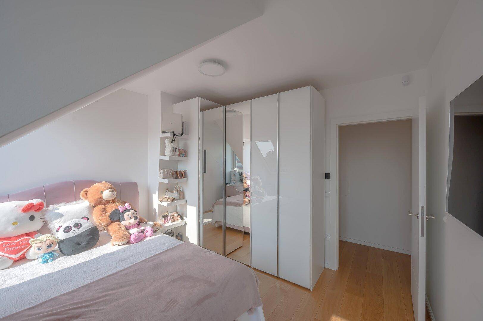 Kinderzimmer mit Bett, Schrank und Dachschräge, hell beleuchtet.