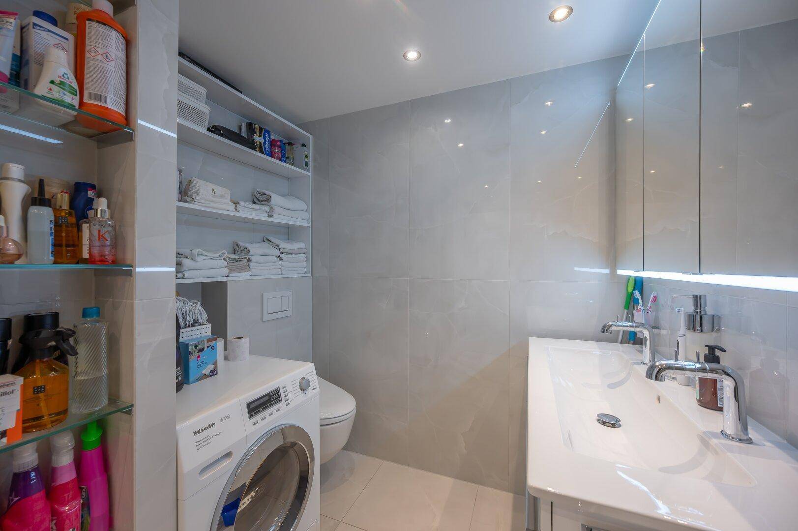Modernes Badezimmer mit Doppelwaschbecken, Waschmaschine und viel Stauraum.